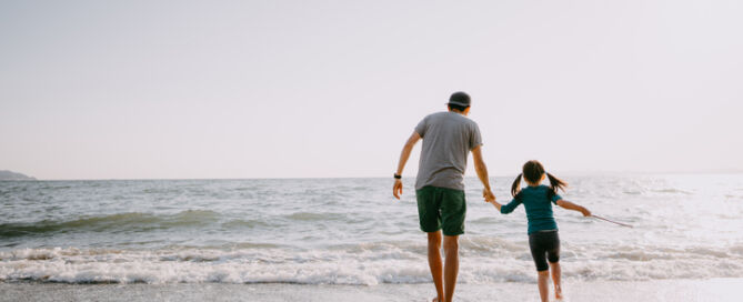 Rear View Of Father And Child Walking On Beach