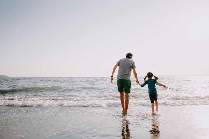 Rear View Of Father And Child Walking On Beach
