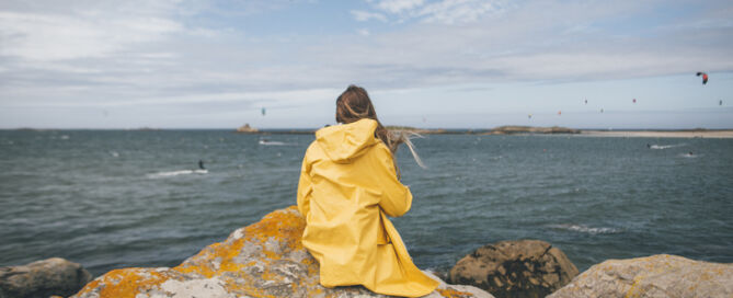 France, Brittany, Landeda, Dunes De Sainte Marguerite, Young Woman Sitting On Rock At The Coast