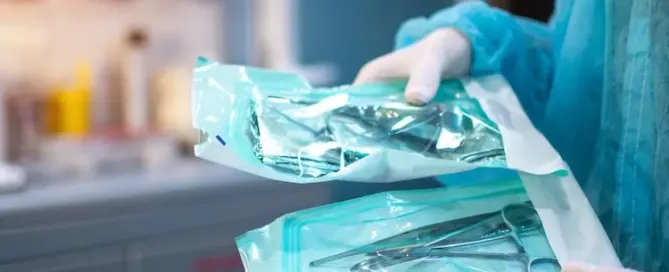 Nahaufnahme von Zahnarzthänden in weißen sterilen Handschuhen mit zahnärztlichen Werkzeugen für den chirurgischen Einsatz verpackt in einer Schutzfolie aus Kunststoff
