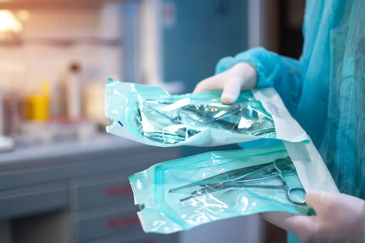 Nahaufnahme von Zahnarzthänden in weißen sterilen Handschuhen mit zahnärztlichen Werkzeugen für den chirurgischen Einsatz verpackt in einer Schutzfolie aus Kunststoff